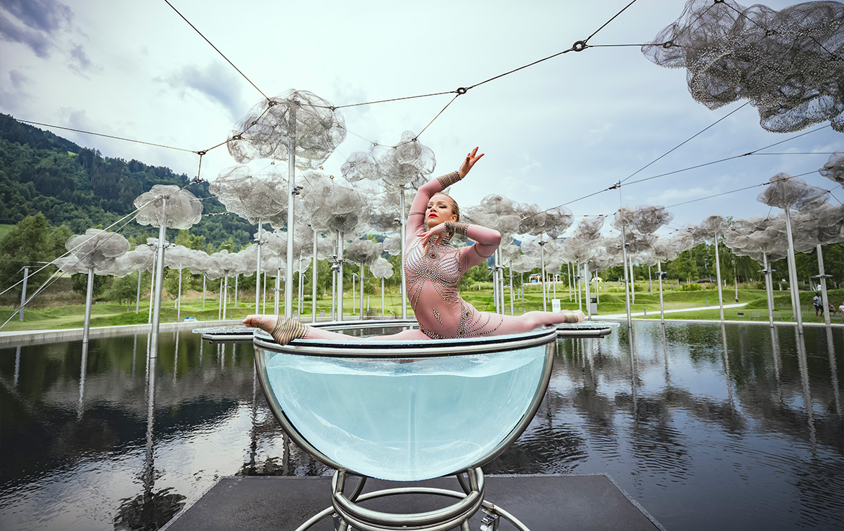 A water ballet acrobat performs a balancing act on her large bowl of water against the backdrop of the crystal cloud above the mirror lake