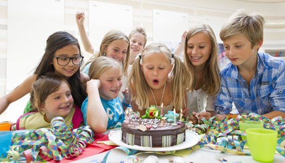 Mädchen bläst umrundet von Kindern Geburtstagskerzen auf einer Torte aus
